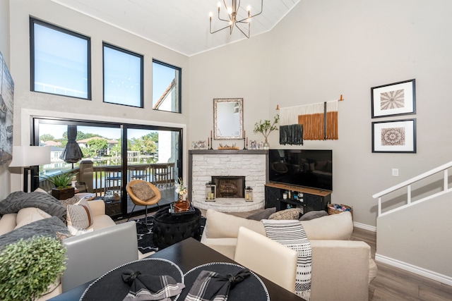 living room featuring a stone fireplace, hardwood / wood-style floors, a chandelier, and a high ceiling