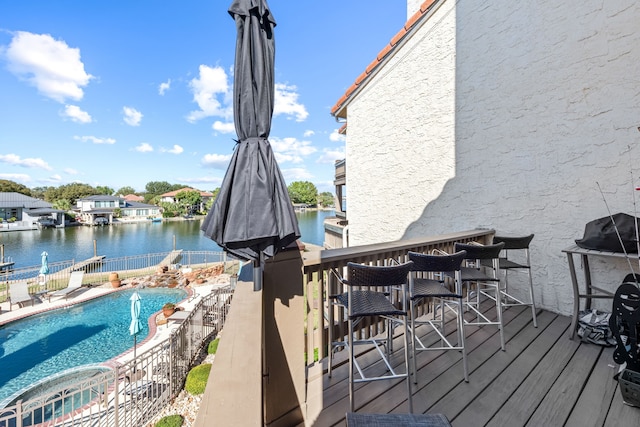 wooden deck with a fenced in pool, an outdoor bar, and a water view