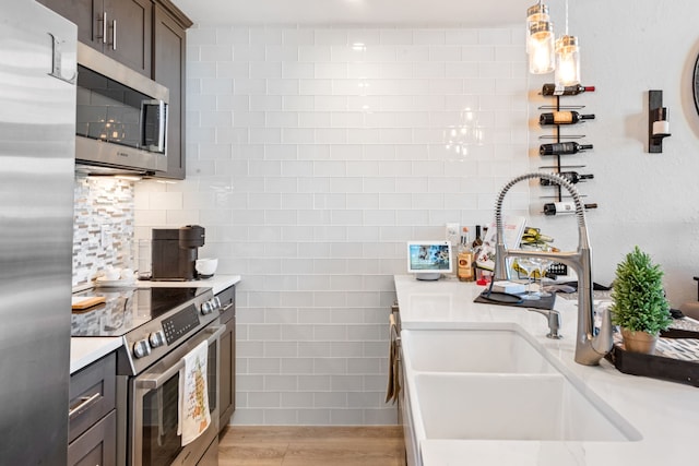 kitchen with appliances with stainless steel finishes, dark brown cabinetry, sink, light hardwood / wood-style flooring, and hanging light fixtures