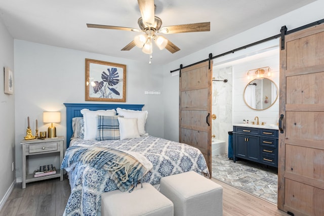 bedroom featuring a barn door, ensuite bathroom, ceiling fan, and light hardwood / wood-style floors