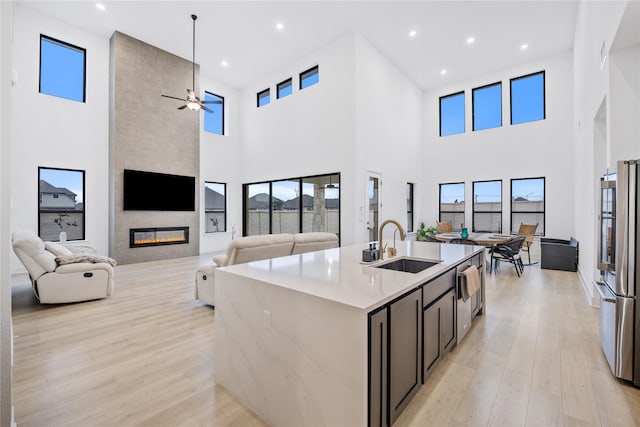 kitchen featuring appliances with stainless steel finishes, light wood-type flooring, a fireplace, a high ceiling, and an island with sink