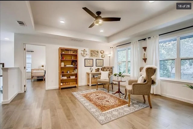 sitting room featuring ceiling fan, hardwood / wood-style floors, and a raised ceiling