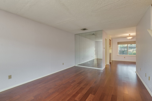 unfurnished room with a textured ceiling and dark wood-type flooring