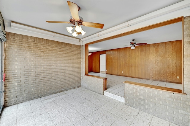 unfurnished room with ceiling fan, wood walls, and brick wall