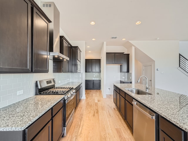 kitchen with light hardwood / wood-style floors, light stone countertops, appliances with stainless steel finishes, sink, and wall chimney range hood