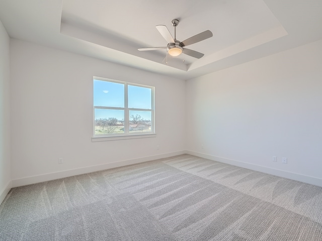 carpeted empty room with ceiling fan and a raised ceiling