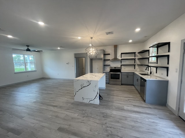 kitchen with appliances with stainless steel finishes, wall chimney exhaust hood, ceiling fan with notable chandelier, sink, and hanging light fixtures