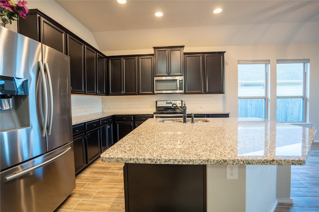 kitchen with sink, light stone counters, a center island with sink, appliances with stainless steel finishes, and decorative backsplash