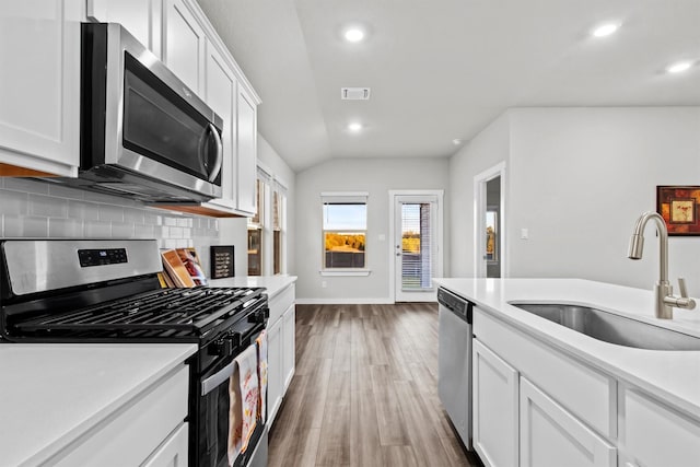 kitchen featuring sink, stainless steel appliances, tasteful backsplash, lofted ceiling, and white cabinets