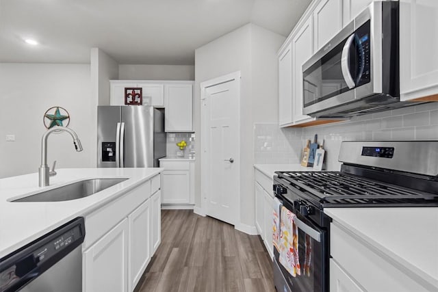 kitchen featuring sink, white cabinetry, hardwood / wood-style flooring, stainless steel appliances, and backsplash