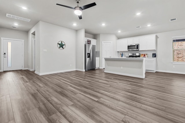 kitchen featuring a kitchen island with sink, ceiling fan, light wood-type flooring, appliances with stainless steel finishes, and white cabinetry