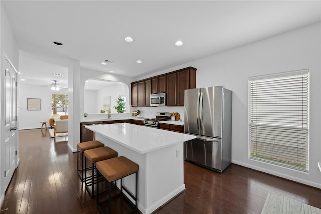 kitchen featuring dark brown cabinetry, a center island, dark hardwood / wood-style flooring, a breakfast bar area, and appliances with stainless steel finishes