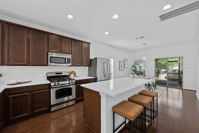 kitchen with a kitchen breakfast bar, appliances with stainless steel finishes, decorative light fixtures, a kitchen island, and dark hardwood / wood-style flooring