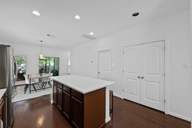 kitchen with dark wood-type flooring, decorative light fixtures, stainless steel refrigerator, and a kitchen island