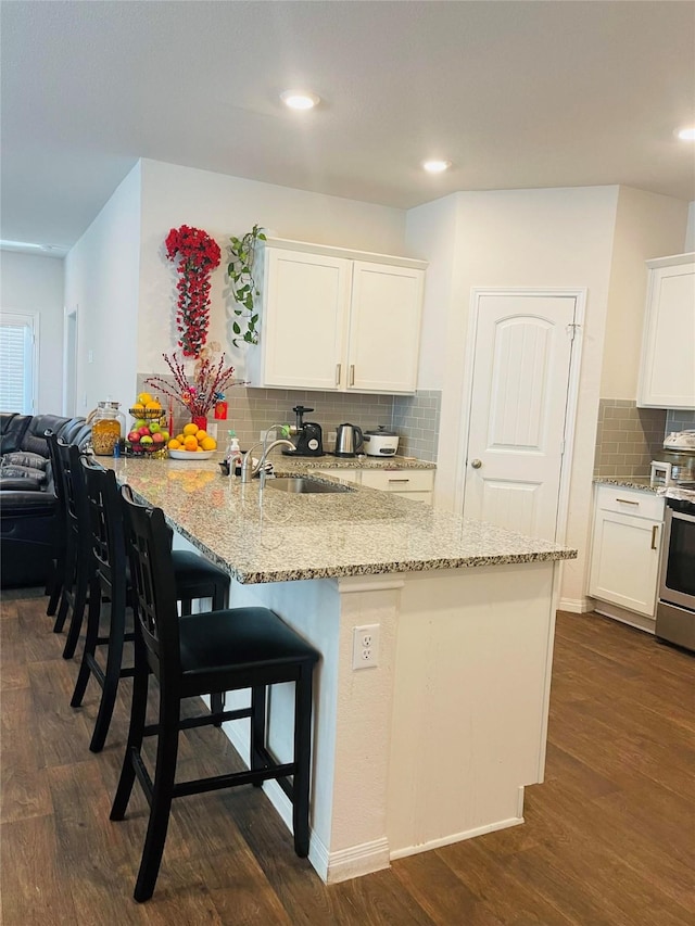 kitchen featuring kitchen peninsula, dark hardwood / wood-style flooring, light stone counters, white cabinets, and a breakfast bar area