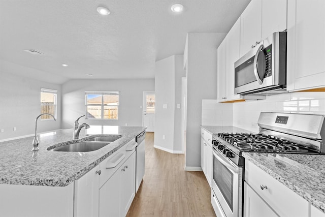 kitchen with a center island with sink, sink, light stone countertops, appliances with stainless steel finishes, and white cabinetry