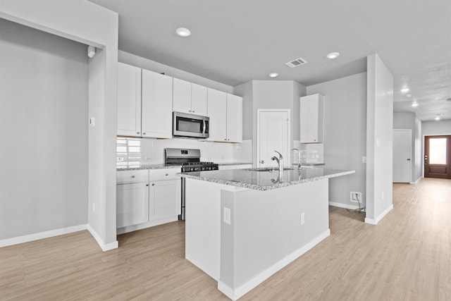 kitchen with a kitchen island with sink, light stone counters, white cabinetry, and stainless steel appliances