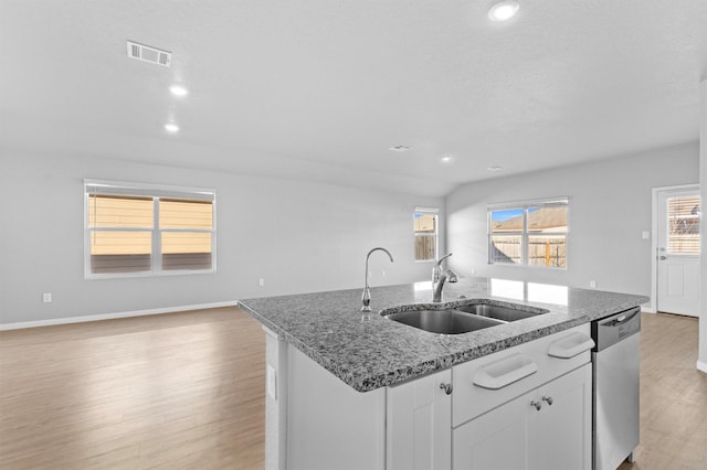 kitchen with dishwasher, a kitchen island with sink, sink, stone countertops, and white cabinetry