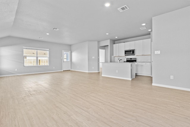 unfurnished living room with light wood-type flooring, a textured ceiling, and vaulted ceiling