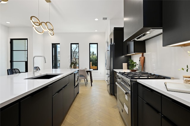 kitchen featuring high end appliances, wall chimney range hood, sink, light parquet flooring, and hanging light fixtures