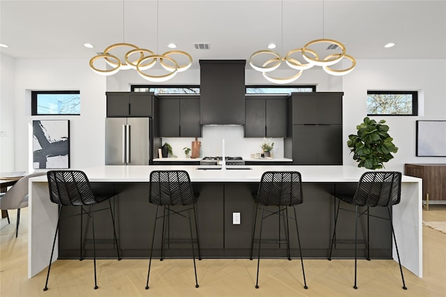 kitchen with stainless steel fridge, a breakfast bar, extractor fan, a large island with sink, and hanging light fixtures