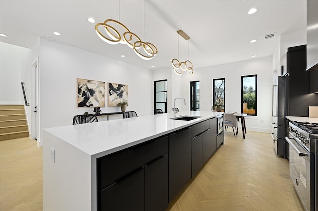 kitchen featuring sink, stainless steel appliances, a large island with sink, decorative light fixtures, and light parquet flooring