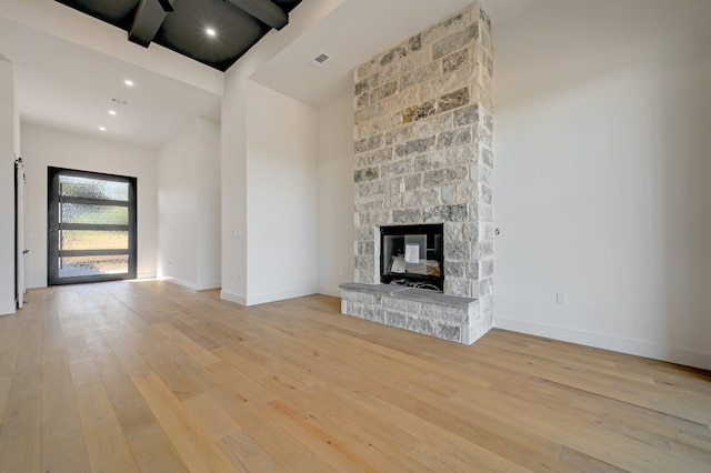 unfurnished living room featuring a towering ceiling, a fireplace, and light hardwood / wood-style flooring