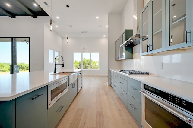 kitchen with stainless steel appliances, a kitchen island with sink, sink, light hardwood / wood-style floors, and hanging light fixtures