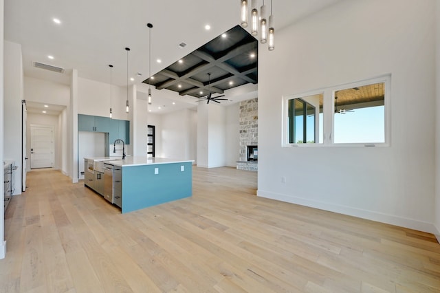 kitchen with a kitchen island with sink, ceiling fan, light hardwood / wood-style flooring, a stone fireplace, and hanging light fixtures