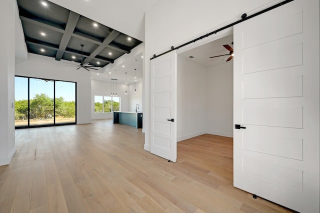 empty room with a high ceiling, coffered ceiling, a barn door, light wood-type flooring, and beamed ceiling