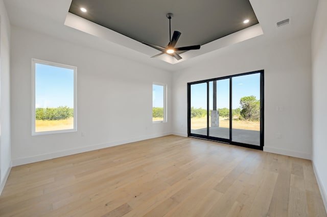 empty room with light wood-type flooring, a tray ceiling, and ceiling fan