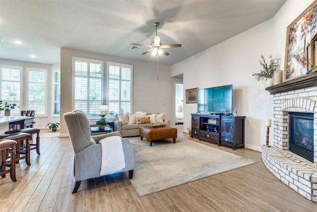 living room with ceiling fan, a fireplace, and light hardwood / wood-style flooring