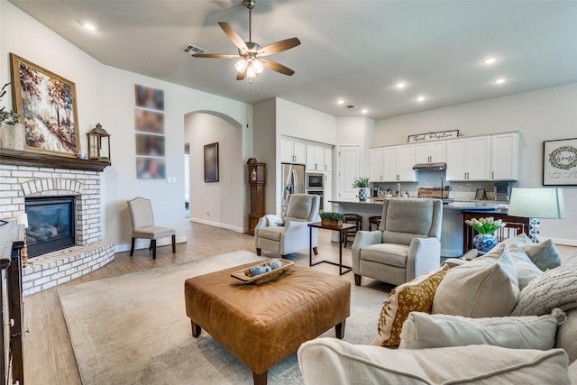 living room featuring a fireplace, light wood-type flooring, and ceiling fan