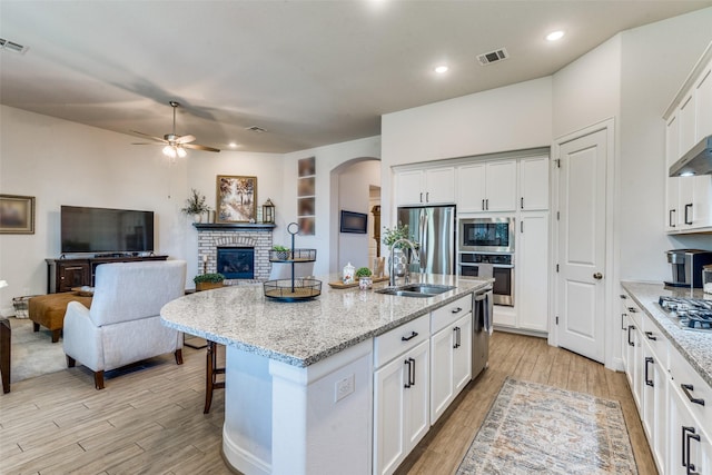 kitchen featuring a center island with sink, white cabinets, sink, appliances with stainless steel finishes, and light stone counters