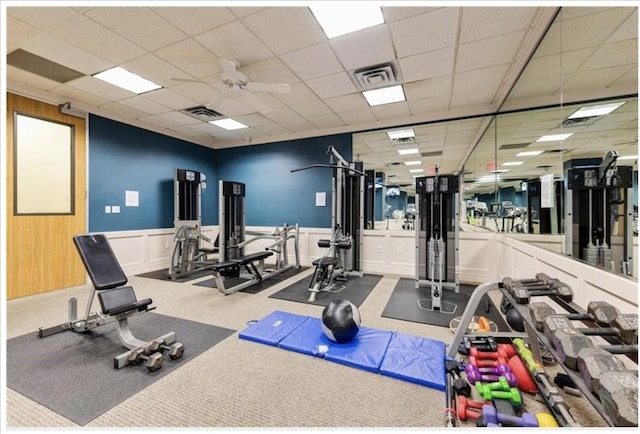 workout area with a paneled ceiling, ceiling fan, carpet floors, and wooden walls