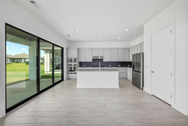 kitchen with white cabinets, decorative backsplash, an island with sink, and appliances with stainless steel finishes