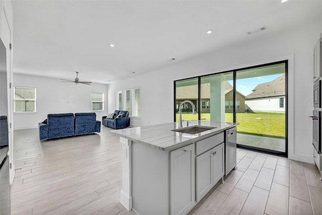 kitchen featuring light stone countertops, stainless steel appliances, sink, a center island with sink, and white cabinetry