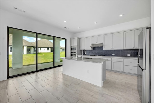 kitchen featuring decorative backsplash, stainless steel appliances, sink, a center island with sink, and white cabinets