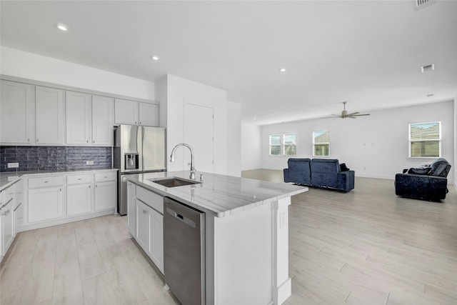 kitchen featuring a kitchen island with sink, sink, ceiling fan, light stone counters, and stainless steel appliances