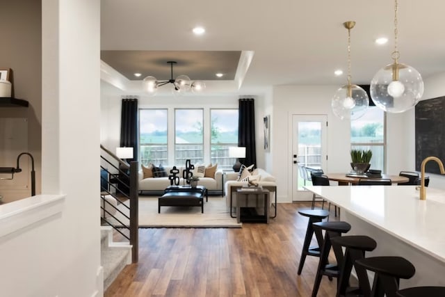 kitchen with hardwood / wood-style floors, a breakfast bar, pendant lighting, a tray ceiling, and an inviting chandelier