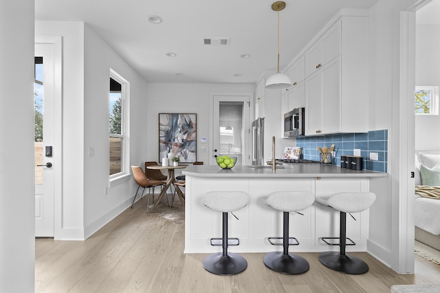 kitchen with kitchen peninsula, pendant lighting, decorative backsplash, a kitchen bar, and white cabinets