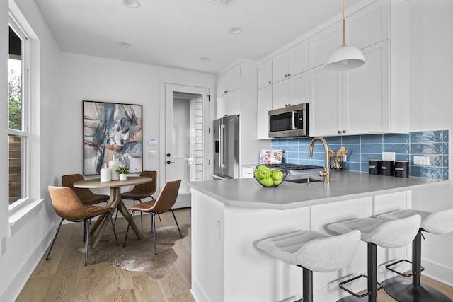 kitchen with white cabinetry, light wood-type flooring, decorative backsplash, pendant lighting, and appliances with stainless steel finishes