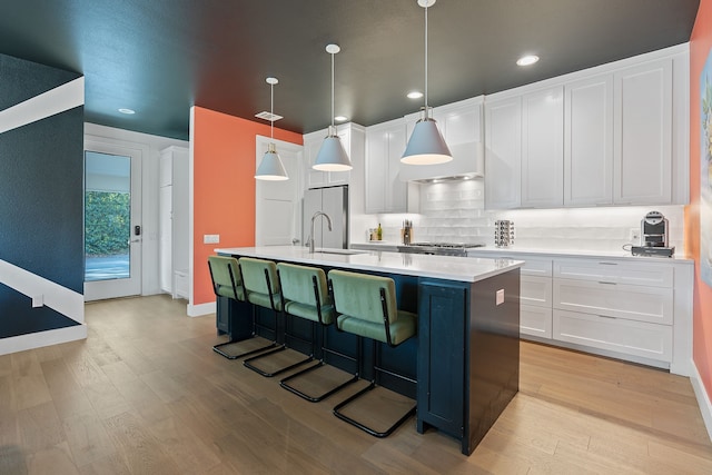 kitchen featuring tasteful backsplash, sink, pendant lighting, white cabinets, and an island with sink