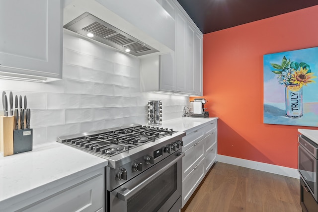 kitchen featuring dark wood-type flooring, white cabinets, stainless steel stove, decorative backsplash, and wall chimney exhaust hood