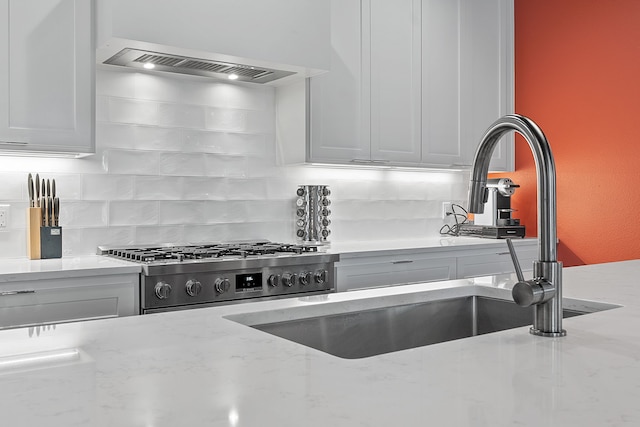 kitchen featuring white cabinetry, wall chimney range hood, tasteful backsplash, light stone counters, and range