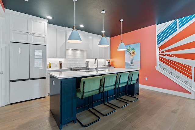 kitchen featuring pendant lighting, a center island with sink, white cabinets, white refrigerator, and light hardwood / wood-style flooring