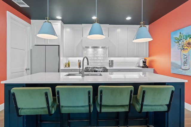 kitchen with hanging light fixtures, hardwood / wood-style flooring, white cabinets, and a kitchen island with sink