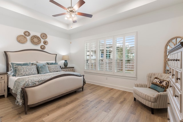 bedroom featuring light wood-type flooring, ceiling fan, and a raised ceiling