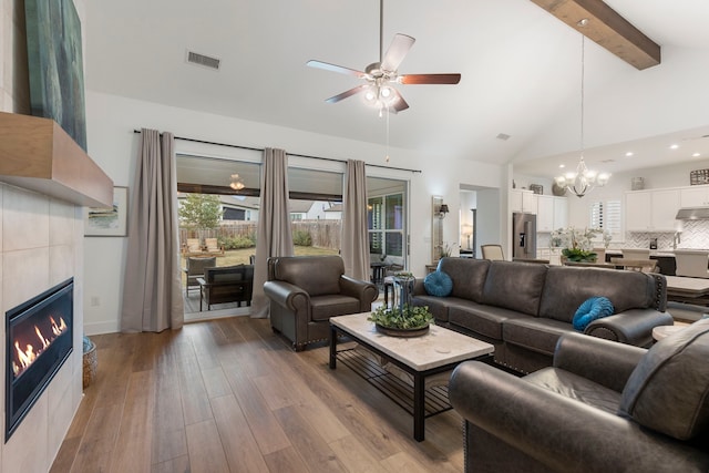 living room with a tiled fireplace, light hardwood / wood-style floors, a wealth of natural light, and beamed ceiling