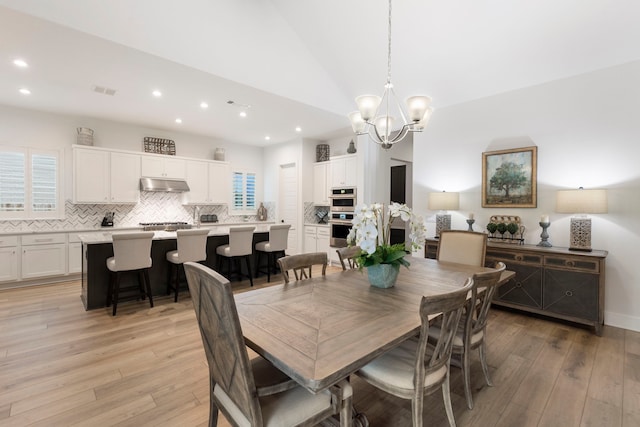 dining space featuring light wood-type flooring, vaulted ceiling, and a chandelier